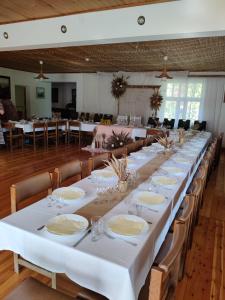 einen langen Tisch mit weißen Tischen und Stühlen in einem Zimmer in der Unterkunft Pilskalni in Īvande