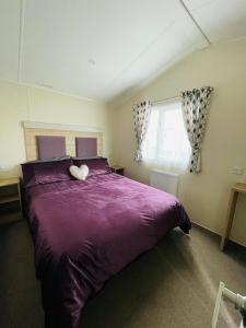 Un dormitorio con una cama morada con un animal de peluche. en Water Sky Getaways 3-bedroom caravans at Durdle Door, en Wareham
