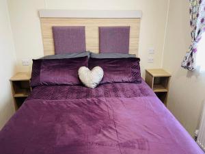 a bed with a purple comforter with a heart pillow at Water Sky Getaways 3-bedroom caravans at Durdle Door in Wareham