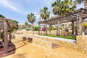 a patio with a stone wall and a wooden pergola at Relax, vacaciones y lujo a 15 metros del mar in Arenales del Sol
