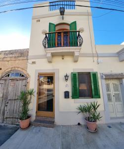 a white house with green shutters and a balcony at Ramla Boutique Home in Marsaskala