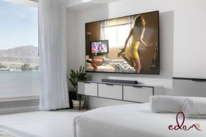 a living room with a tv and a woman in a yellow dress at סוויטה משפחתית מרווחת עם נוף לים - By Edomlux in Eilat
