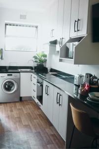 a kitchen with white cabinets and a washer and dryer at Designer Luxe Stellies Studio in Stellenbosch