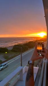 una persona tomando una foto de la puesta de sol en Quequen frente al mar con pileta climatizada en Quequén