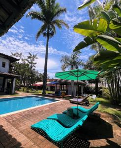 uma piscina com 2 espreguiçadeiras e um guarda-sol verde em Pousada Casa Paradiso Guarujá no Guarujá