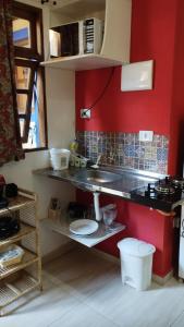 a kitchen with a sink and a red wall at Chalé de Charme MANDOMAI - Suítes com Cooktop e Chalé Charmoso com Cozinha in Ilhabela