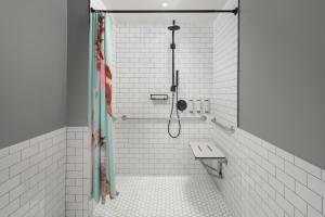 a shower in a white tiled bathroom with a bench at Moxy Houston Downtown in Houston