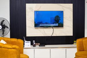 een flatscreen-tv aan een muur met twee stoelen bij Apartment B16 in Port Harcourt