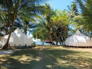 two white tents on a beach with palm trees at Firesky Glamping Ocam Ocam Beach in New Busuanga
