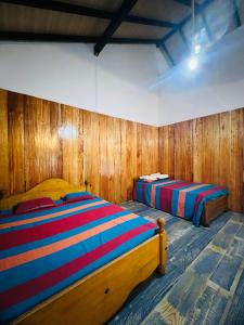 two beds in a room with wooden walls at Anaas Motel in Deniyaya