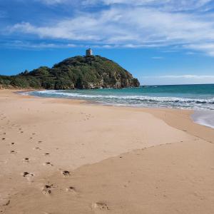 a beach with footprints in the sand with a lighthouse on an island at La Rosa dei Venti B&B in Chia