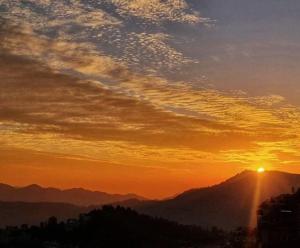 a sunset with the sun setting on a mountain at The Breeze Homestay in Shimla