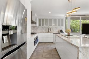 La cuisine est équipée de placards blancs et d'un réfrigérateur en acier inoxydable. dans l'établissement Luxury spacious 3-bedroom Suite on exclusive Lansell Rd, Toorak, à Melbourne