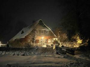 a house covered in snow at night with lights at Reetdachhaus, Wilstermarsch in Landscheide