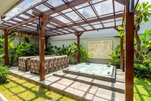 eine Terrasse mit einem Whirlpool unter einer hölzernen Pergola in der Unterkunft Tranquility Manor Bali in Sanur