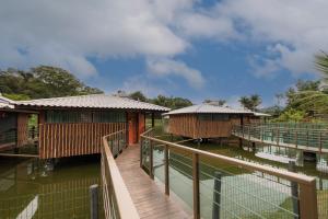 a wooden walkway leading to two buildings on water at Pousada Dona Carmita in Brumadinho