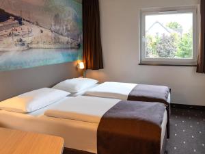 two beds in a hotel room with a window at B&B Hotel Koblenz in Koblenz