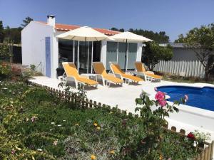 a pool with chairs and umbrellas next to a house at Monte da Palmeirinha in Vila Nova de Milfontes