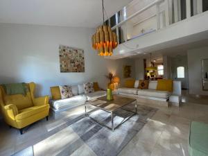 a living room with couches and a table and yellow chairs at Private Villa in Quinta da Marinha with golf view! in Cascais
