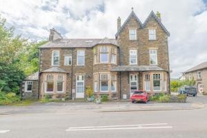 une grande maison en briques avec une voiture rouge garée devant dans l'établissement Enjoy relaxing family breaks in this central Ambleside apartment with parking, à Ambleside