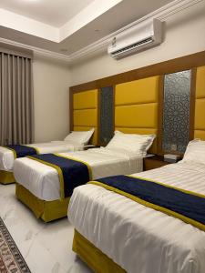 Cette chambre d'hôtel comprend 3 lits avec des draps jaunes et bleus. dans l'établissement HOLIDAy فاملي الطائف, à Taif