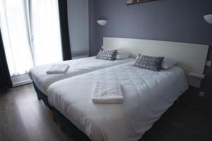 2 camas en una habitación con sábanas y almohadas blancas en Hôtel des Dunes Noirmoutier, en La Guérinière