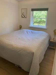 1 cama blanca en un dormitorio con ventana en Moderne sommerhus i naturskønne omgivelser, en Gedser