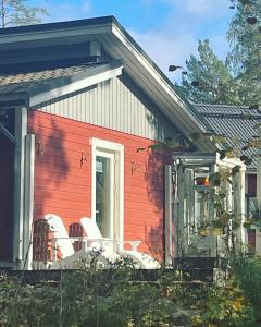 une maison rouge avec 2 chaises sur la terrasse couverte dans l'établissement Vuolenkosken Helmi - laadukas ympärivuotinen kohde, à Huutotöyry