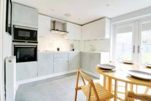 a white kitchen with a wooden table and chairs at Recently renovated,modern house. train station in North Mimms