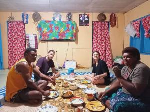 un grupo de personas sentadas alrededor de una mesa con comida en Lusis Homestay, en Lautoka