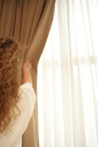 a woman with curly hair looking out of a window at Troci Hotel in Tirana