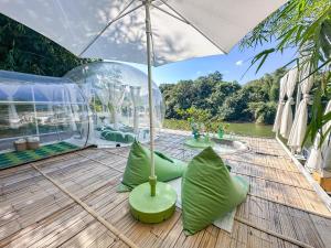a patio with an umbrella and green pillows on a wooden deck at The Three Bubble Houses in Sai Yok +38 photos