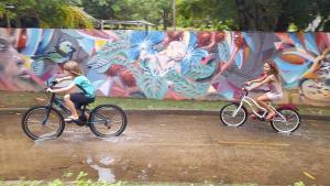 two girls riding bikes in front of a mural at Casona de Barro in Imbassai