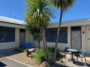 un edificio con 2 palmeras, mesa y sillas en Academy Motor Inn, en Tauranga