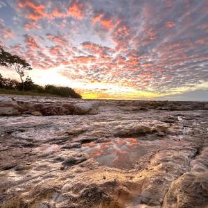 un tramonto su una spiaggia rocciosa con un cielo nuvoloso di Unit 3 Golden Sands Retreat a Wagait Beach