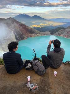 dos hombres sentados en el borde de una montaña tomando una foto en Ijen Transito, en Ketapang