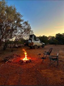 a campfire and two chairs and a truck in a field at Meralda Station in Cobar