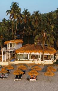 a group of straw umbrellas on a beach with palm trees at Aqua Beach Resort Ashwem in Mandrem