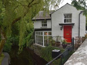 a white house with a red door next to a river at 2 Bed in Cartmel LCC75 in Cartmel