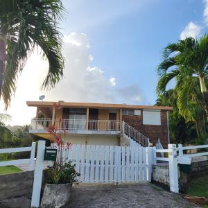 une maison avec une clôture blanche et des palmiers dans l'établissement La Bourgeoisie Créole, à Grande Savane