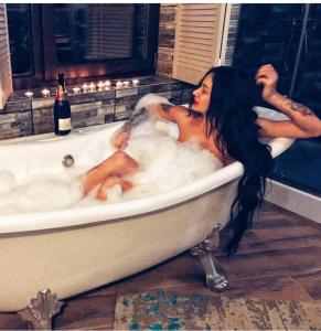una donna sdraiata in una vasca da bagno con una bottiglia di vino di Маєток "ZYMON & SKI" a Bukovel