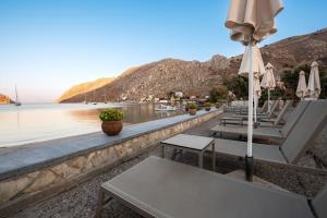 een rij stoelen en parasols naast het water bij Pedi Beach Hotel in Symi