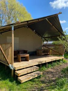 um pavilhão de madeira com uma mesa e bancos num campo em Luxe safaritent aan het water em Hommerts