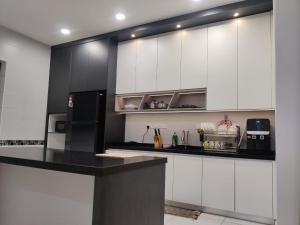 a kitchen with white cabinets and a black refrigerator at 16 Paxs Bungalow Homestay Hutan Melintang by Aloha in Hutan Melintang