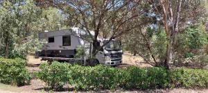 冈尼达RV Caravan in Rural Setting on Edge of Town close to AgQuip的停在树旁田野的卡车