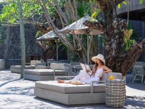 une femme assise sur un canapé qui lit un livre dans l'établissement Peppers Seminyak, à Seminyak