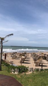 a beach with tables and straw umbrellas and the ocean at Frente al mar con pileta in Quequén