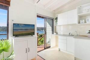 cocina con armarios blancos y TV en la parte superior en Waterfront Scotland Island Holiday Home - Family & Pet Friendly - 3 Bedrooms - Wifi - Netflix - Private Jetty, en Scotland Island