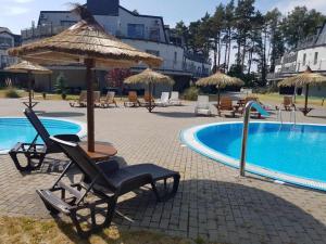 a group of chairs and umbrellas next to a pool at Romantyczny Apartament HAPPY 16 BASEN & KORT TENISOWY, OCHRONA 24 h - dla maksymalnie 6 osób in Pobierowo