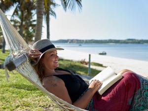 a woman laying in a hammock reading a book at San Martinho Hotel in Vila Praia Do Bilene